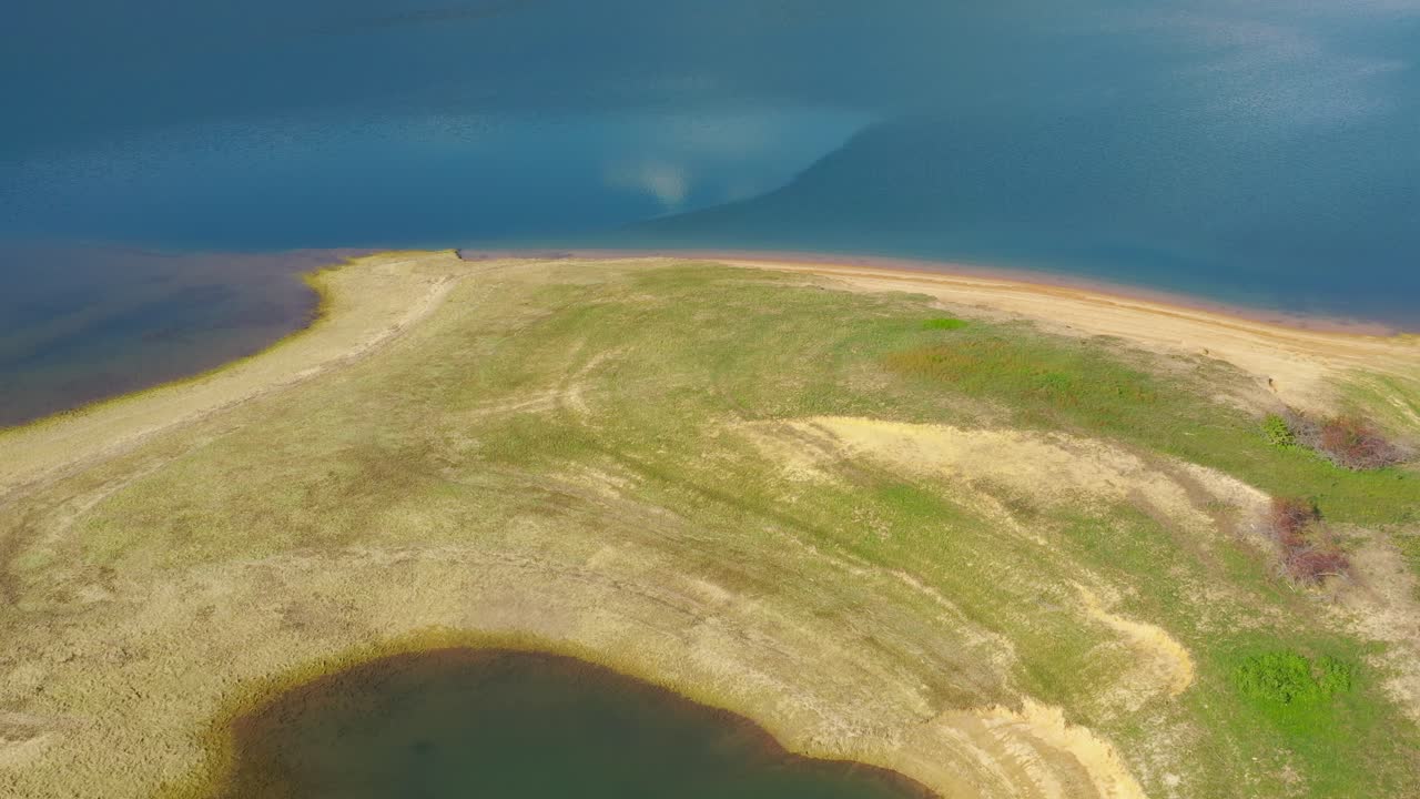 Island with pond in Rama Lake Bosnia and Herzegovina with eroded shore, Aerial flyover shot