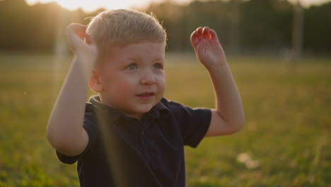 cute little child waves hands on meadow grass at sunset