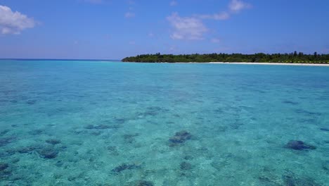 zoom out turquoise waters of the caribbean sea with white beaches covered with palm trees out in the distance, low altitude drone footage in daylight