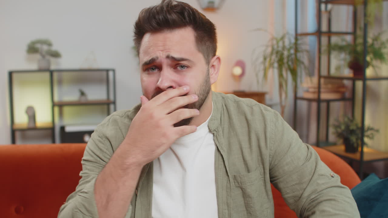 Shocked young man watching tv sitting on sofa feeling hopelessness and loneliness losing match