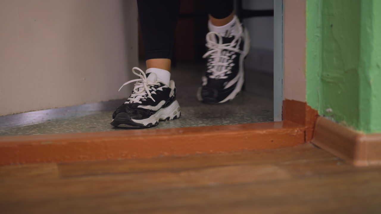 Closeup of legs in black leggings and sneakers walking out through doorway, blurred background highlights casual exit, step captured with focus on footwear, threshold, and indoor setting details