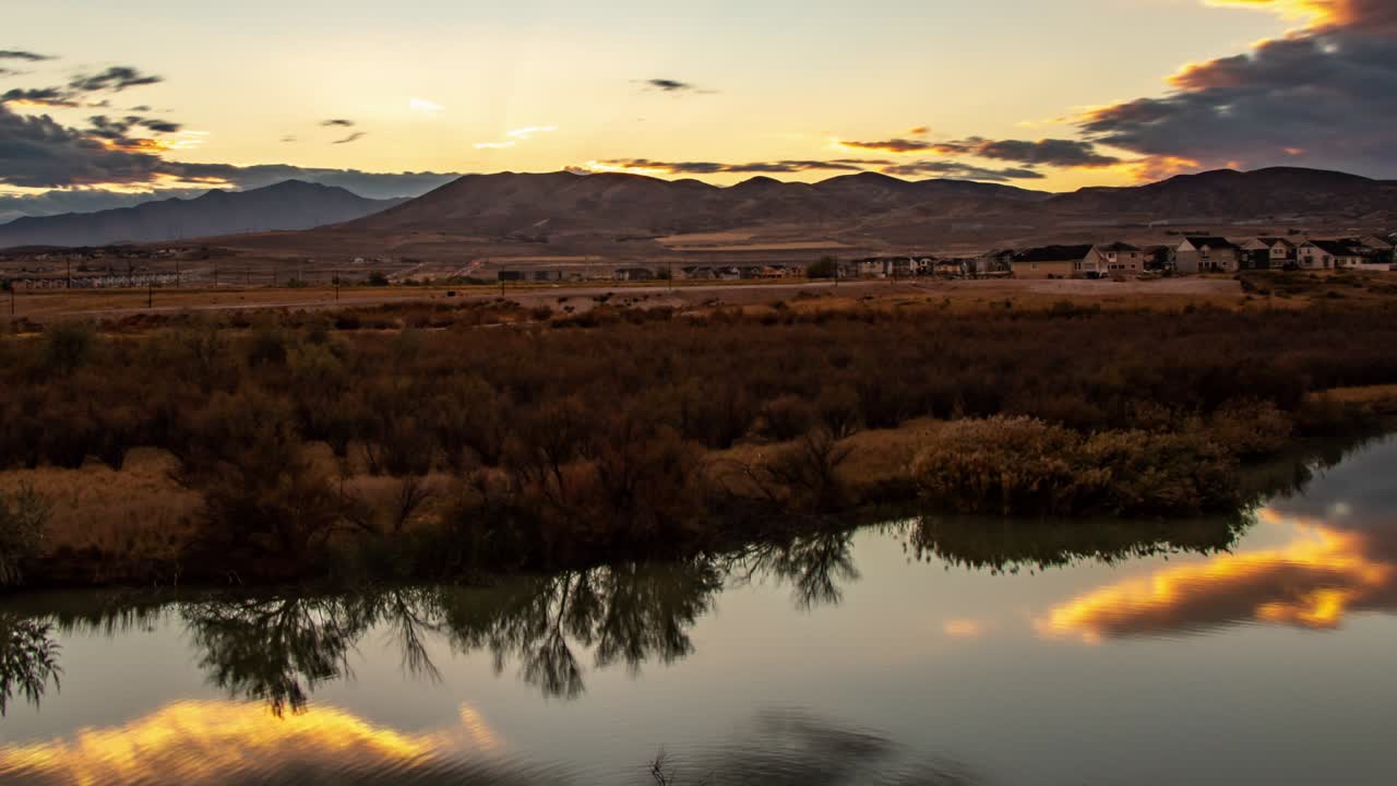 Time-lapse di uno splendido tramonto con un paesaggio nuvoloso che si riflette sulla superficie liscia di un fiume e montagne sullo sfondo - panoramica a sinistra