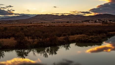 lapso de tiempo de una hermosa puesta de sol con un paisaje nuboso que se refleja en la superficie lisa de un río y montañas en el fondo - paneo a la izquierda