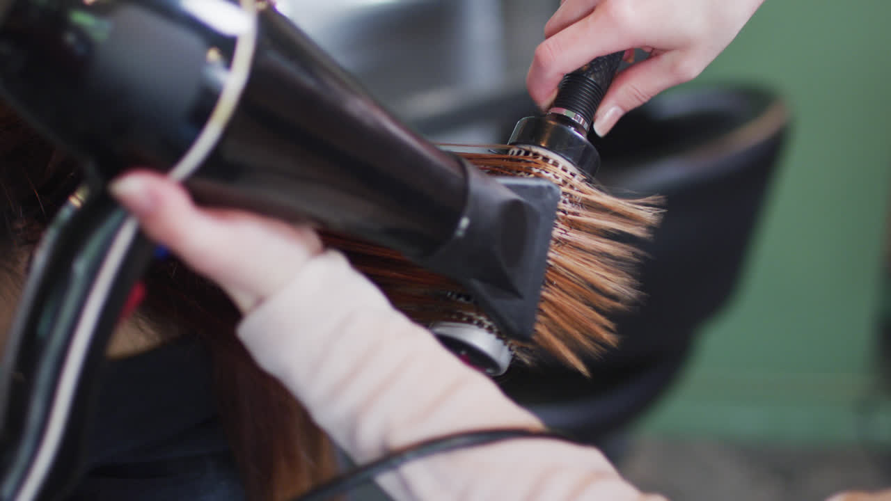Female hairdresser blow drying hair of female customer at hair salon