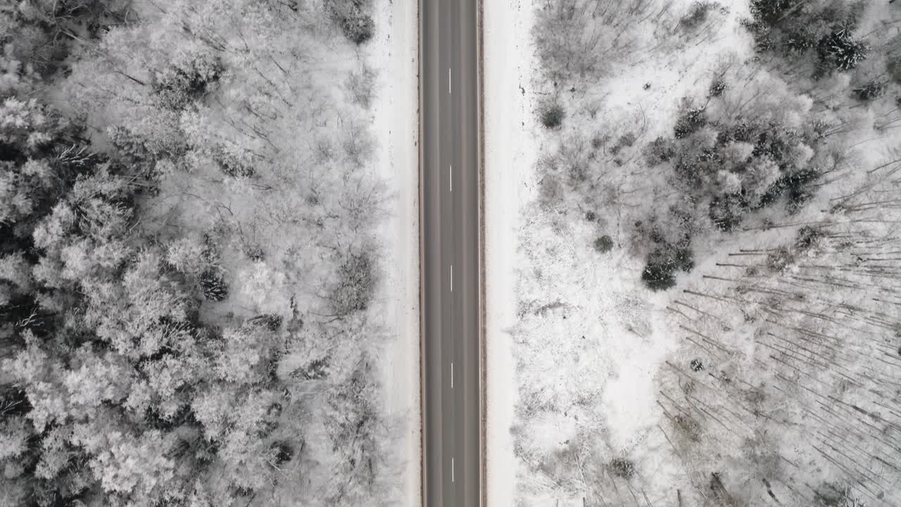 Aerial view of a highway through the forest in winter. Top down drone view of a car driving in countryside with snow covered ground.