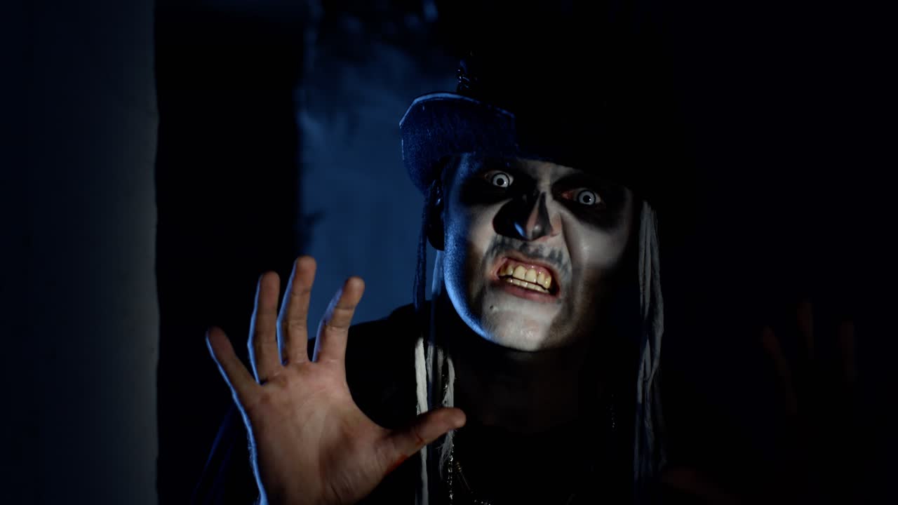 할로윈 스레트 메이크업을 한 무서운 남자가 어두운 모이에서 빠르게 나타나 무서워하려고합니다.