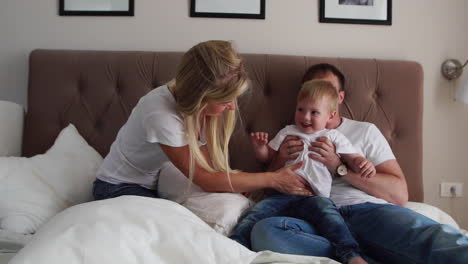 Loving-parents-play-with-their-son-on-the-bed-laughing-and-smiling-in-the-bedroom