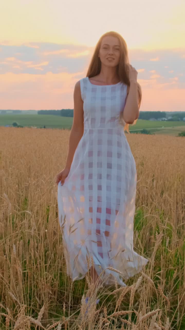 Young woman in flowing white dress dancing in golden wheat field during sunset with vibrant sky