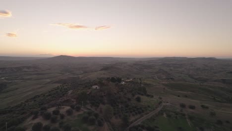 Drone-flying-straight-forward-over-an-Italian-landscape-with-hills,-trees-and-fields-of-grass-in-the-very-early-morning-in-4k