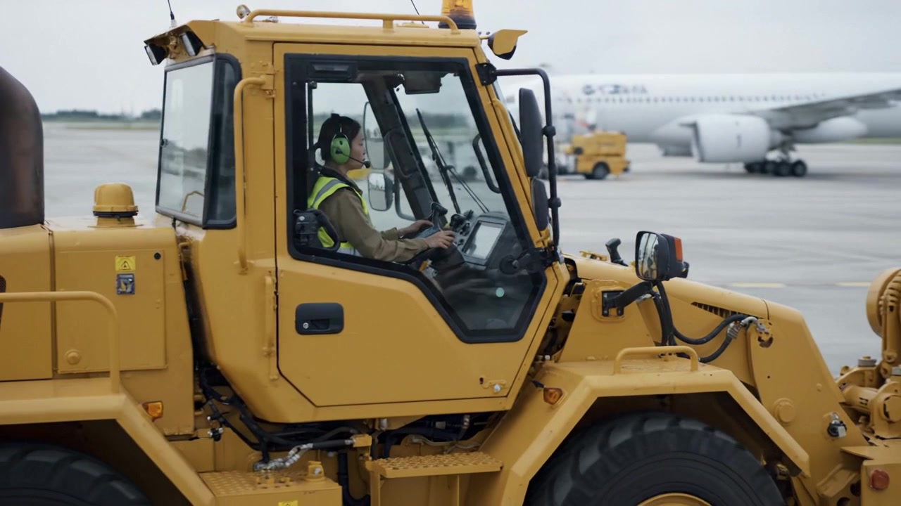 Operational Precision: An Airport Worker Maneuvers a Yellow Tractor on the Tarmac Amidst Aircraft, Showcasing the Dynamic Environment of Air Traffic Management