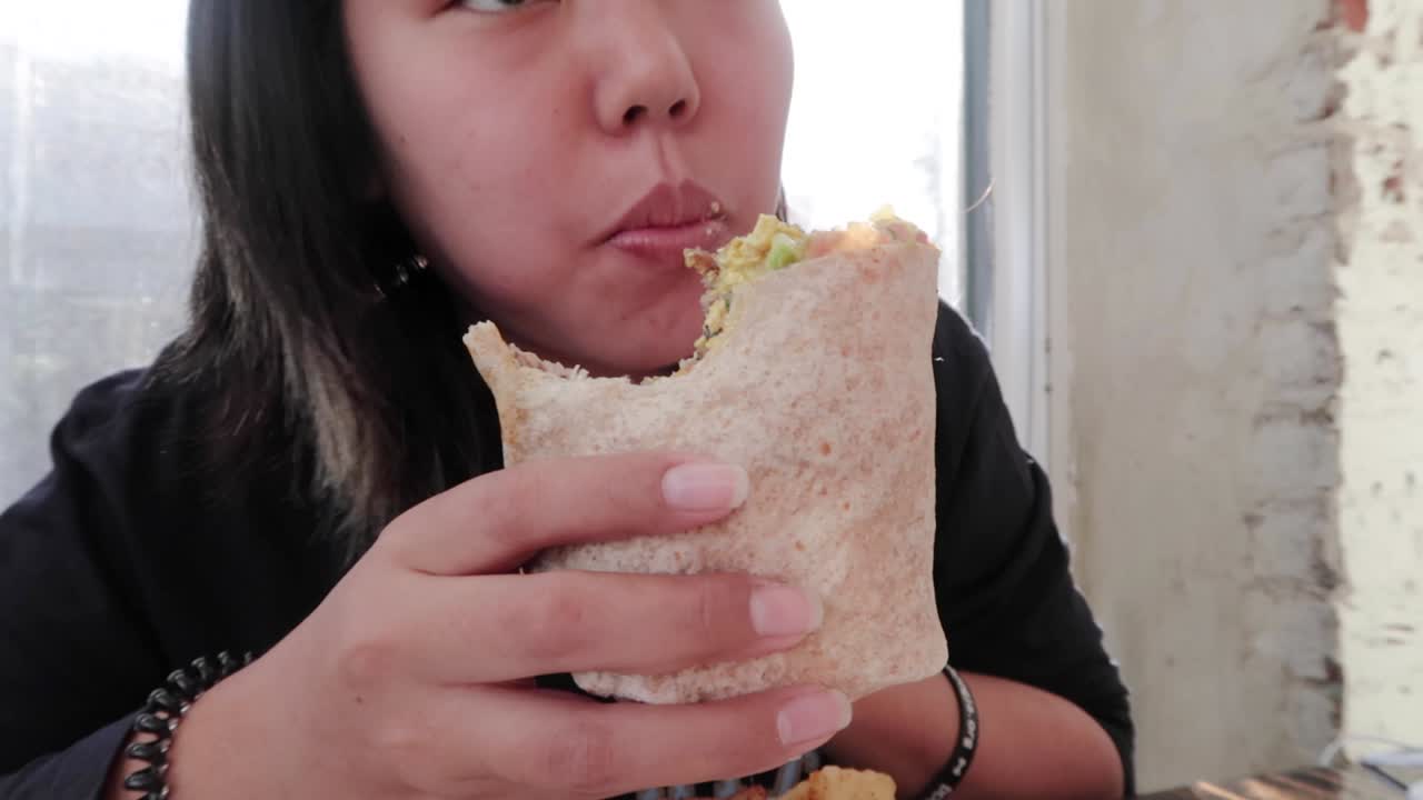 Ragazza vegana che dà un grosso morso a un burrito vegetariano
