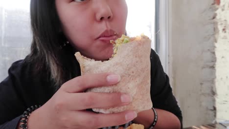 vegan girl eating take a big bite of a veggie burrito