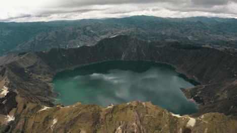 drone shot of beautiful crater lake with green color surrounded by volcano in ecuador - birds eye view