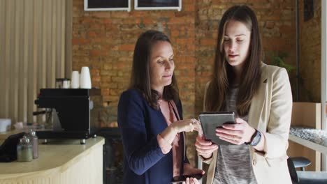 Caucasian-female-business-owner-and-her-coworker-using-tablet-and-talking