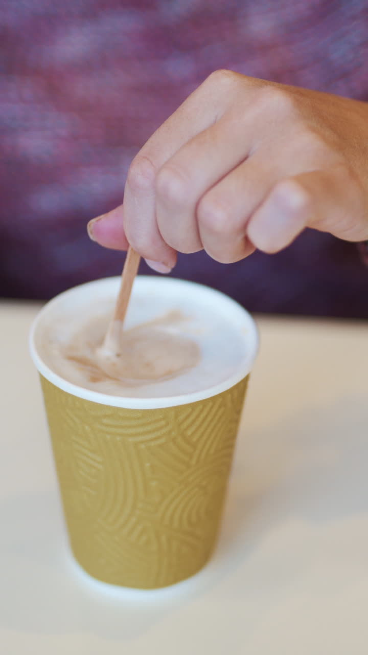 Woman adding sugar and mixing coffee in cafe. Coffee break in cafe. Hot drink in paper cup Vertical video