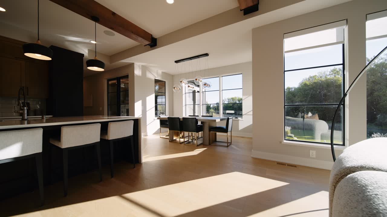 A modern dining area with a sleek table, pendant lighting, and large windows, filled with natural light