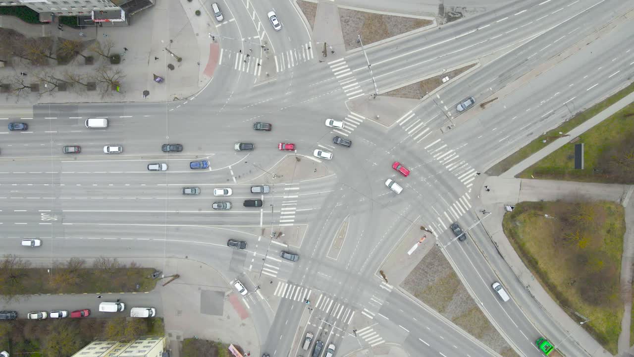 Top down aerial view of Kristiine intersection in Tallinn Estonia where cars, vehicles and truck drive forward and turn. zebra and road crossing are visible with white markings and green grass visible