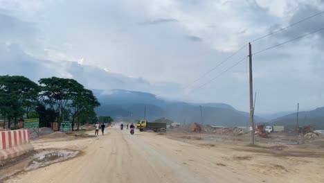 Driving-along-a-dirt-road-into-oncoming-traffic-while-a-huge-truck-turns-onto-the-road-in-Bholaganj-Bangladesh