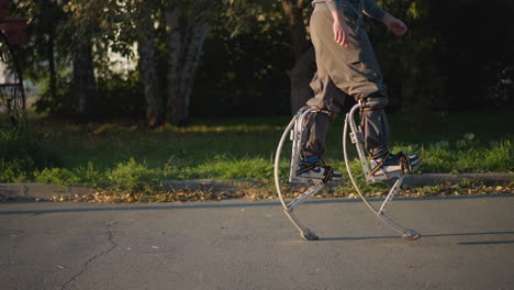 guy walking with stilts wearing gray hoodie and pants on paved road surrounded by green grass and trees, showcasing dynamic movement, balance, and outdoor activity, emphasizing agility