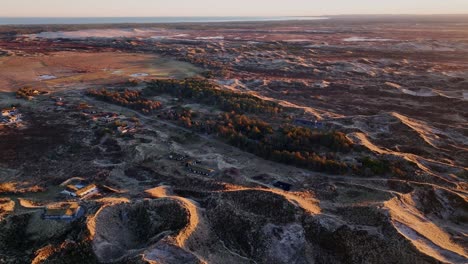 aerial view houses are built between the sand dunes, and the dunes are illuminated by the yellow color of the sunset.