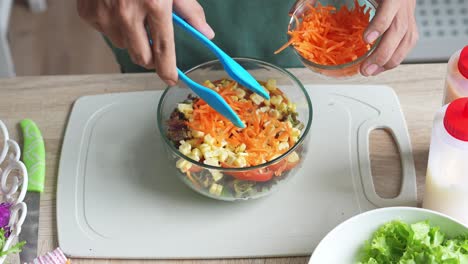 top view of a man hand putting sliced carrots into a salad bowl