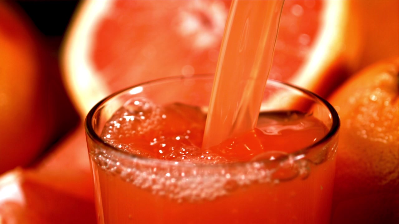 Versare succo di pompelmo fresco in un bicchiere con agrumi.