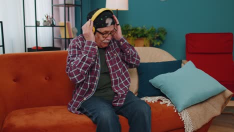 overjoyed senior man in wireless headphones dancing singing on cozy couch in living room at home