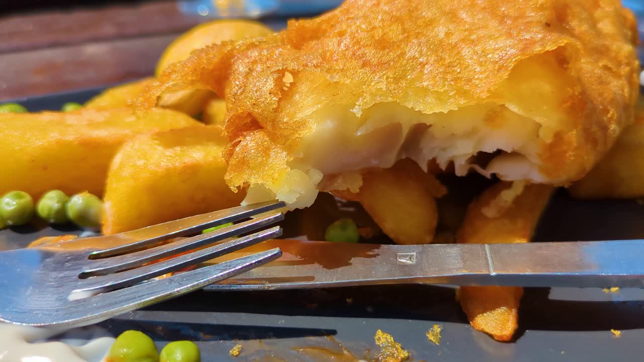 Crossed Over Knife and Fork with Battered Classic Rustic British Fish and Chips Outside During Summer Time. Traditional Fast Food Cuisine.