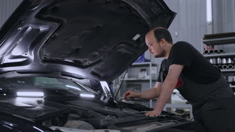 male uses a tablet computer with an augmented reality diagnostics software. specialist inspecting the car in order to find broken components inside. male uses laptop for diagnostics vehicle