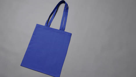 Close-up-of-blue-bag-on-grey-background,-with-copy-space,-slow-motion