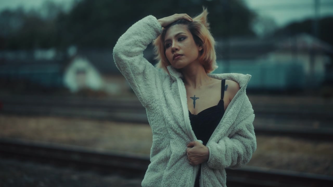 Pensive Young Woman in Fluffy Jacket Standing by Train Tracks