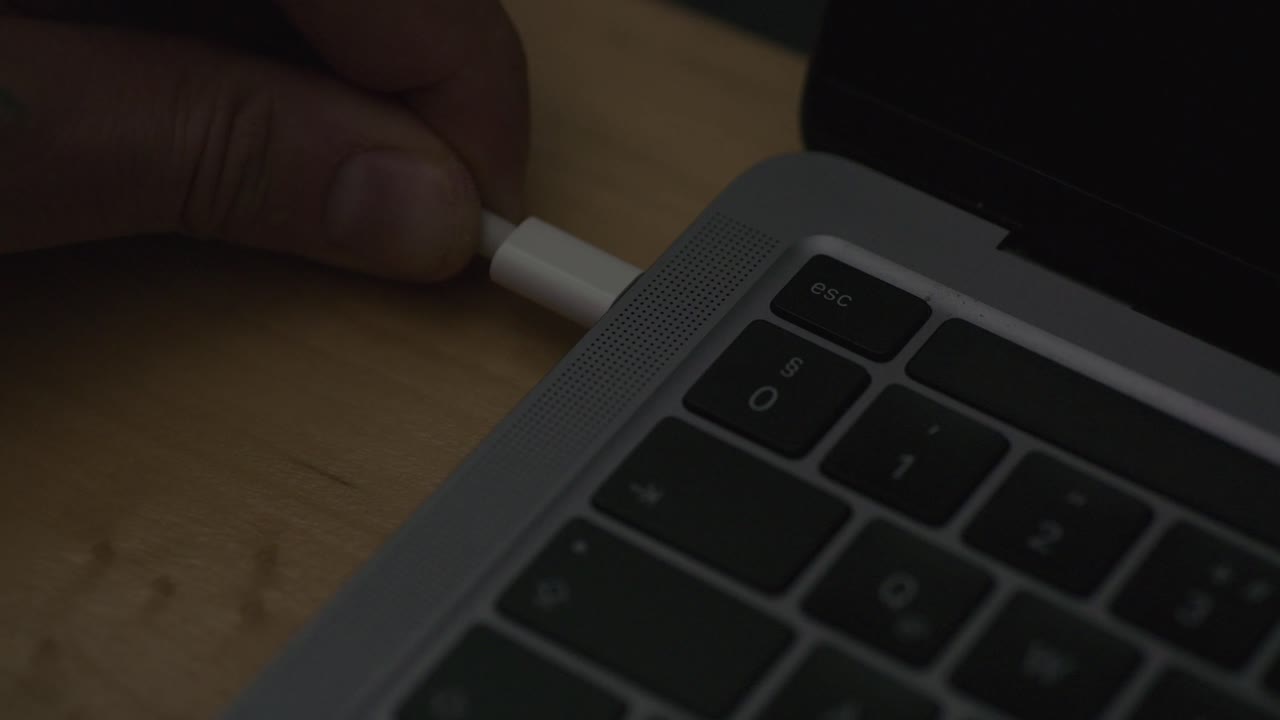 A person’s hand is seen plugging a USB-C cable into the side port of a modern laptop. The close-up shot captures the act of connecting or charging, emphasizing technology and modern digital devices