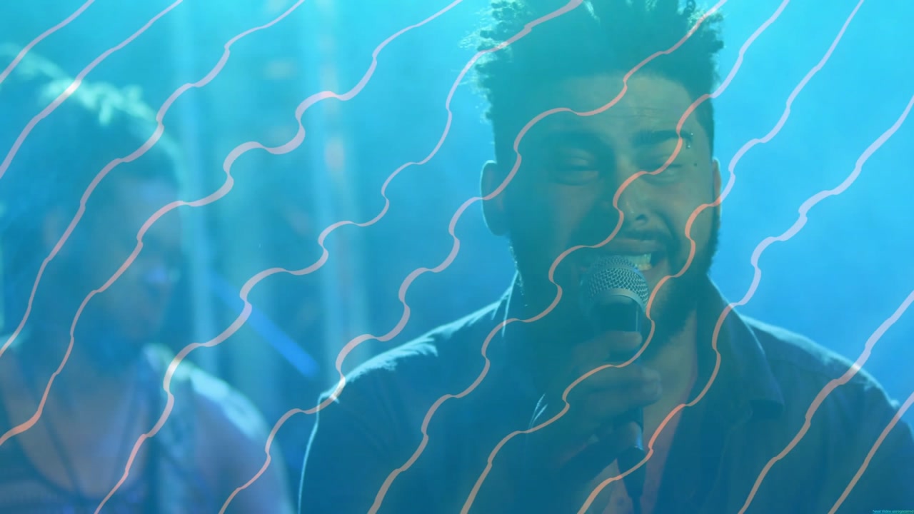 Lead vocalist lifting mic and singing for music crowd, while wavy projection sweeping over faces
