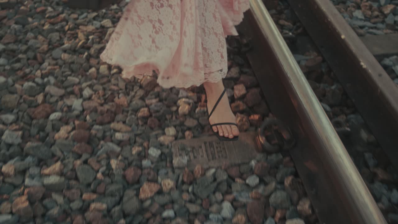 Donna che cammina sui binari del treno con un vestito rosa