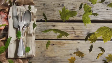 Animation-of-leaves-over-cutlery-and-leaves-on-wooden-background