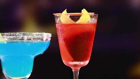 a vibrant display of red and blue cocktails with lemon garnishes, set against a colorful, blurred backdrop.
