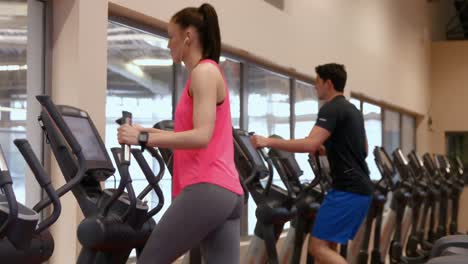 man and woman using the cross trainers in gym