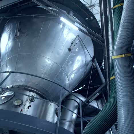 huge dairy tank beside the thick plastic tubes. stainless steel tank standing at the raised platform with sensors at its basics. circle view from below