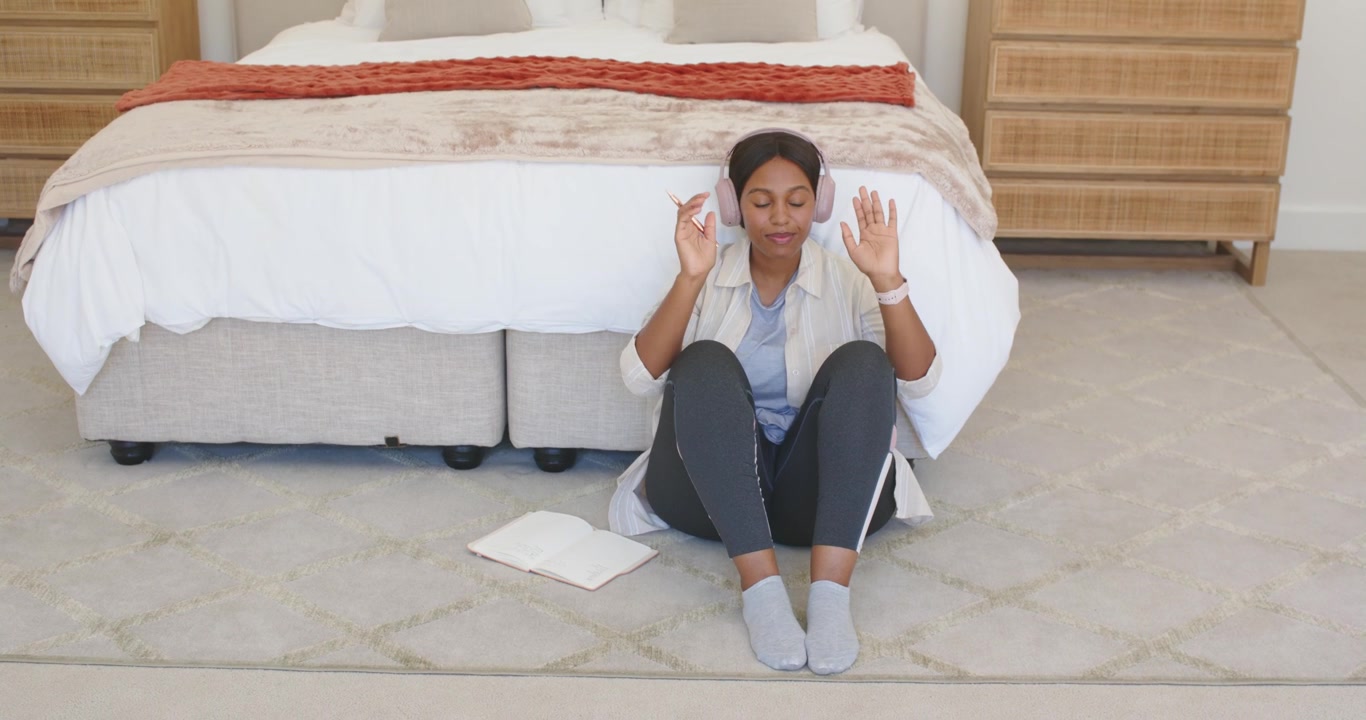 Femme afro-américaine mettant des écouteurs, tapotant sa montre, écoutant avec un ordinateur portable au pied du lit