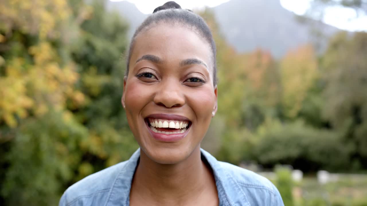 Portrait of happy african american woman looking at camera and smiling in garden, in slow motion