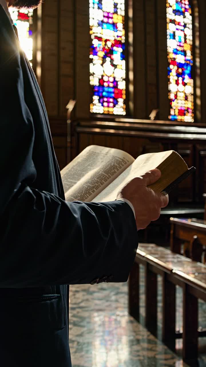 Low-angle shot of a person reading a book in a church, with stained glass windows in the background