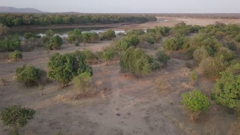 Aerial:-Dirt-road-leads-to-dry-season-river-sand-in-African-bushveld