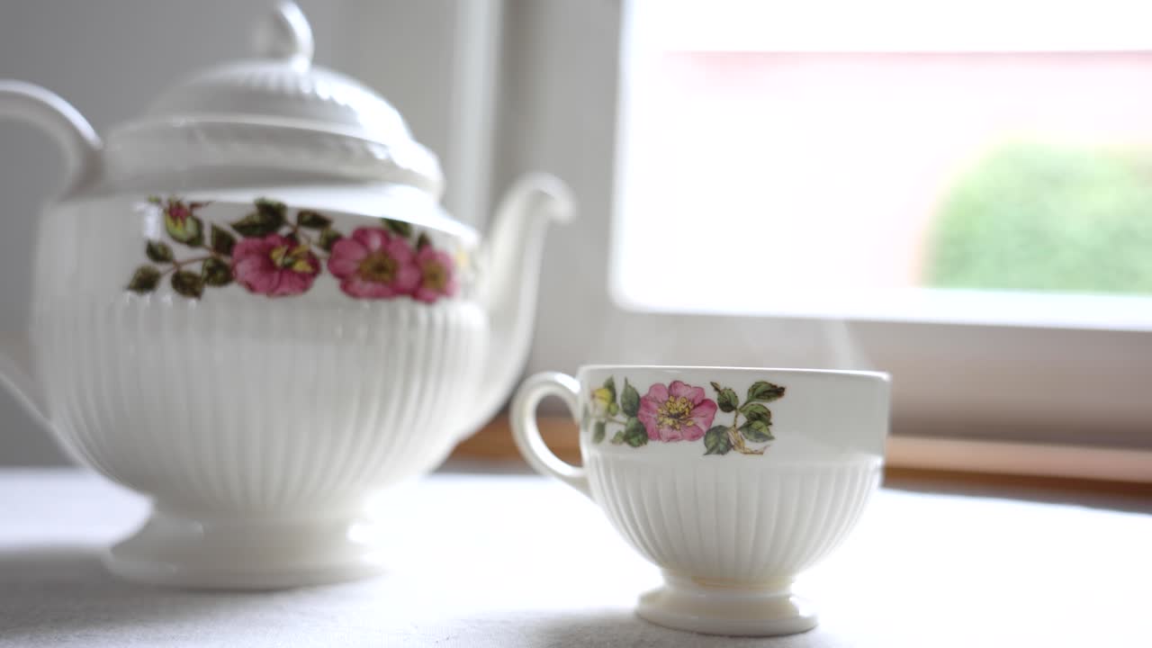 Tè Caldo Fumante in Tazza da Tè Floreale Vintage e Teiera Accanto alla Finestra