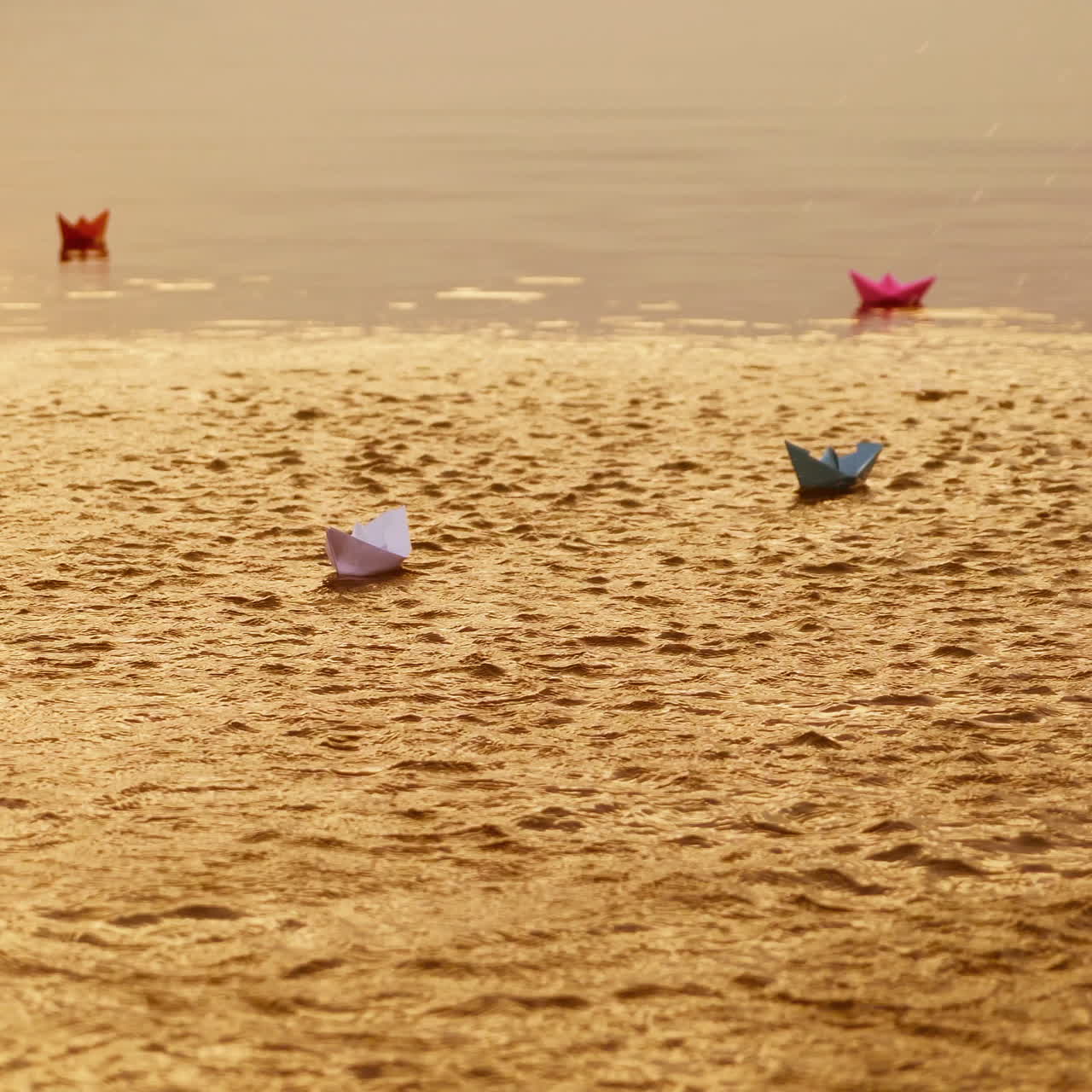 Colored paper ships floating in the river and some water splashes cover them a little at sunset. Four origami boat swim in the water