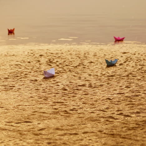 colored paper ships floating in the river and some water splashes cover them a little at sunset. four origami boat swim in the water