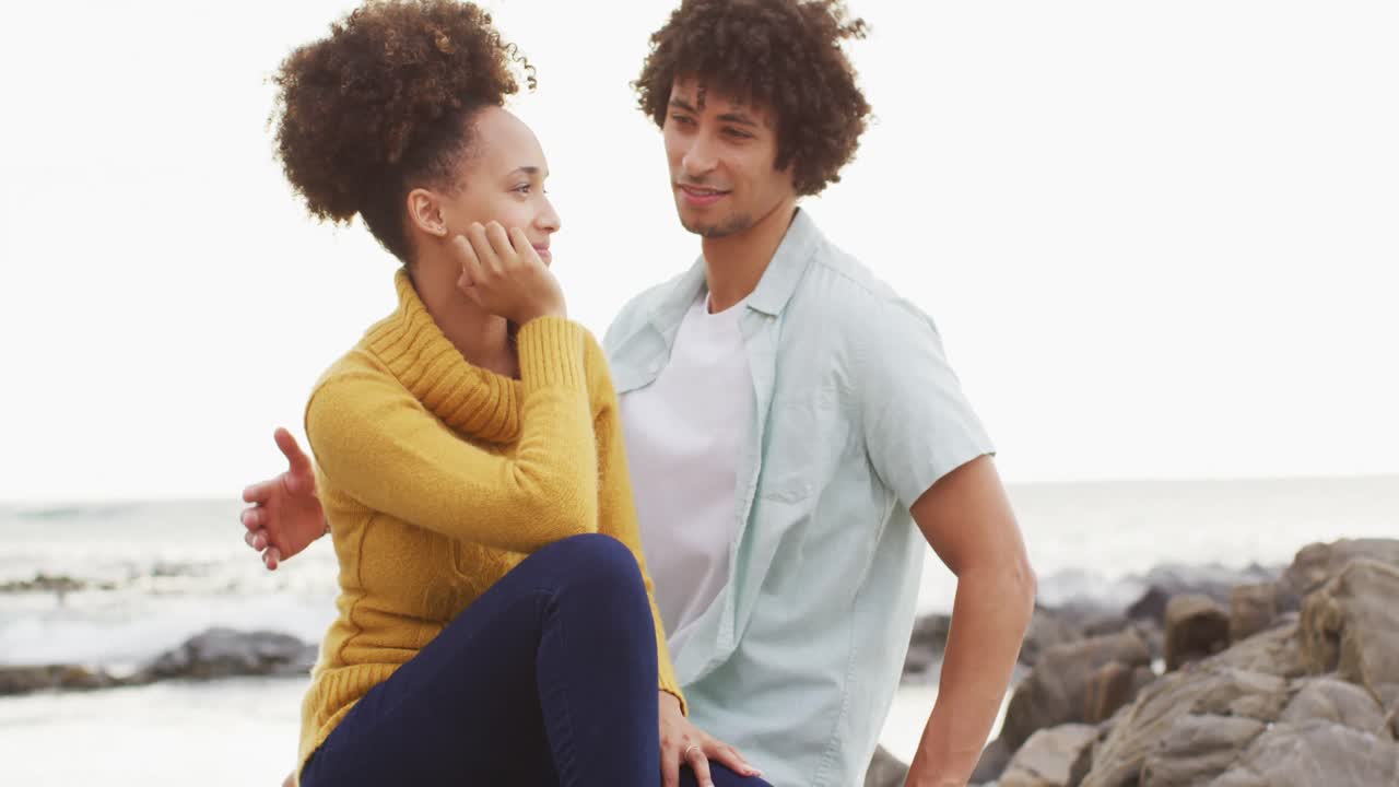 Casal afro-americano abraçando-se sentados nas rochas perto do mar