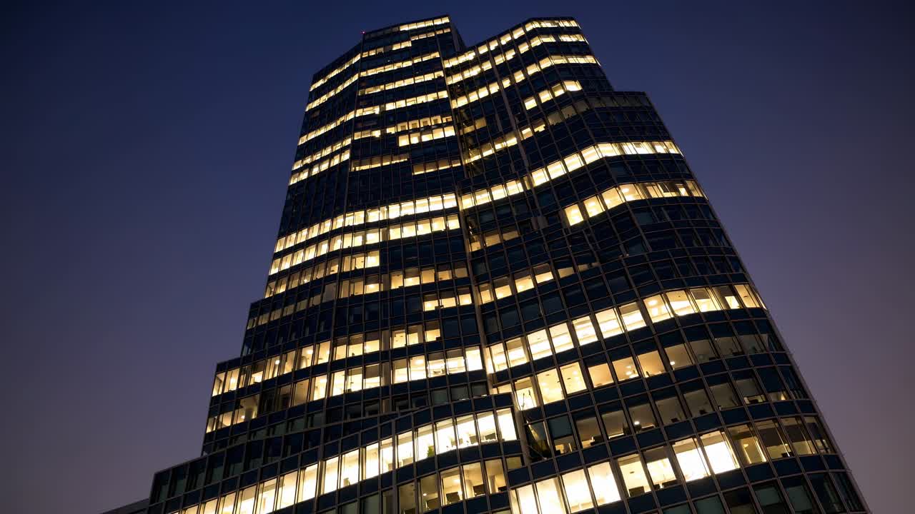 Illuminated windows create a mesmerizing pattern on the dark facade of a modern skyscraper, conveying a sense of activity and progress in the urban landscape at night