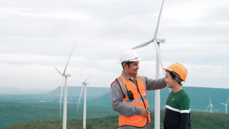 progressive engineer with his son in the wind farm atop of the mountain.