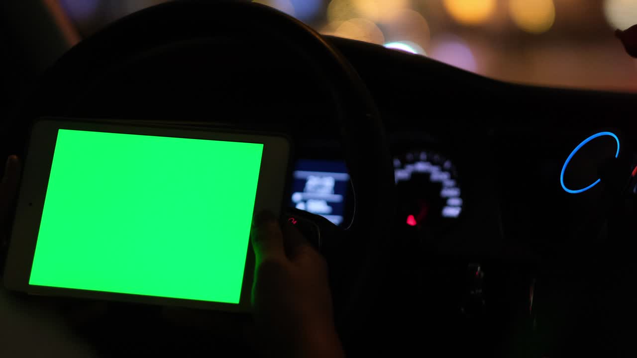 hand holding green screen tablet computer in car at night