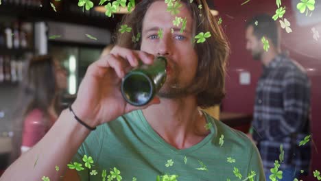 animation of clover icons over caucasian man drinking beer